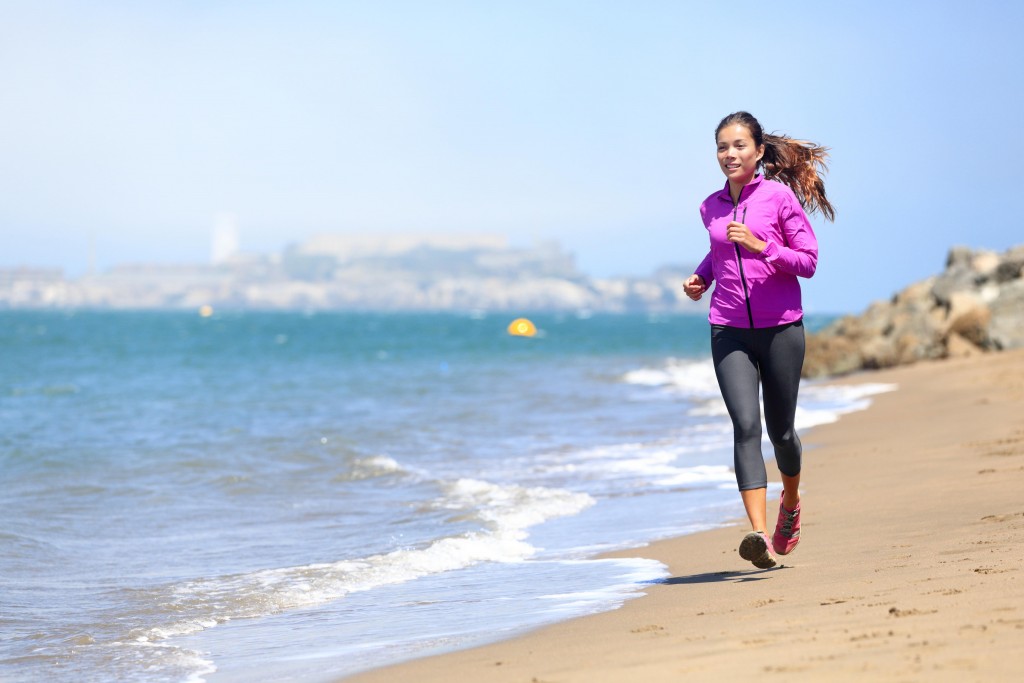 Woman running on San Francisco beach with Alcatraz in background. Smiling happy female athlete runner training on waterfront in San Francisco, California, USA. Mixed race fit fitness sport model.
