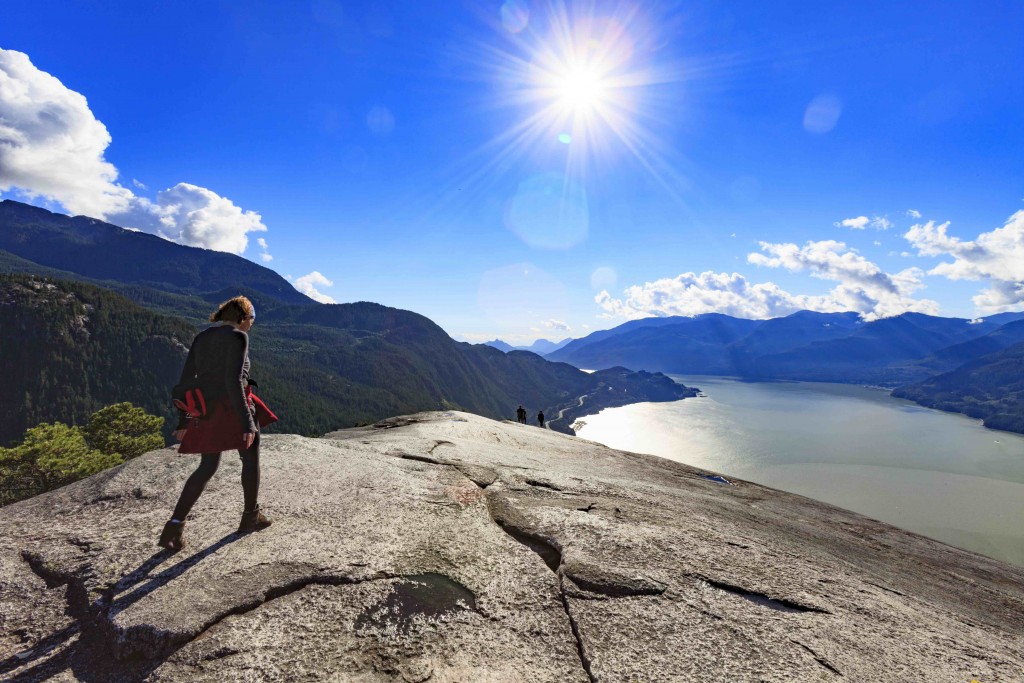A woman walks on the top of “The Chief” a mountain in Squamish British Columbia, Canada with Howe Sound and the coastal mountains in the background.