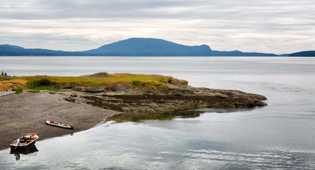 Kayak and motorboat pulled up on the beach of an uninhabited island. Location: San Juan Islands, Washington State USA