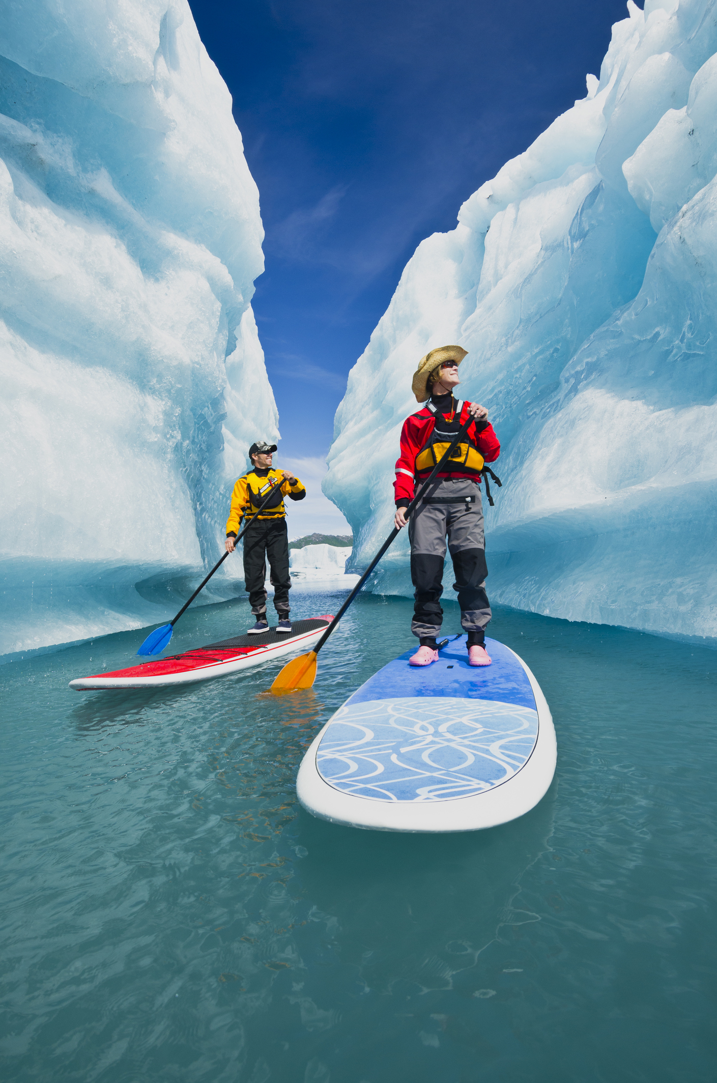 A couple on stand up paddle boards (SUP) explore an iceberg canyon on Bear Lake in Kenai Fjords National Park, Alaska.